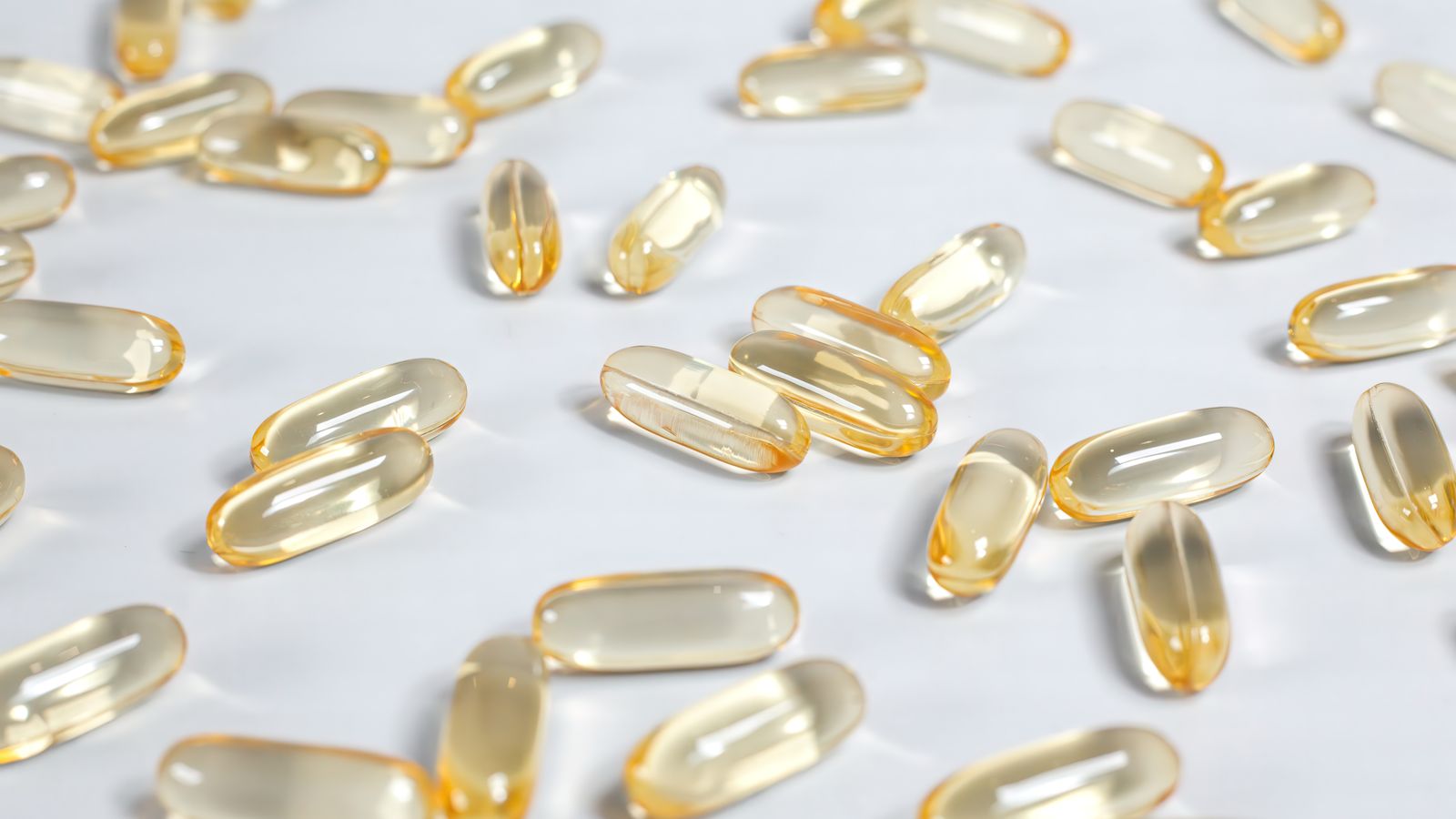 Close-up of yellow transparent softgel capsules on a white background, suitable for pharmaceutical or supplement themes.