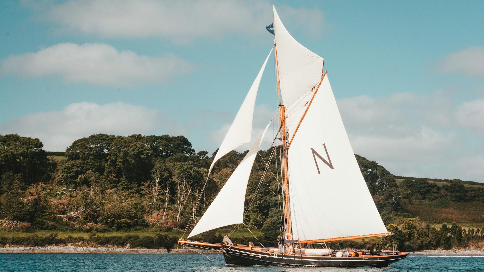A beautiful sailboat gliding through the waters near the lush Falmouth coastline.