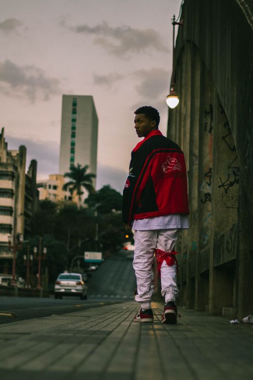 Free Stylish man in red jacket walks through urban Brazilian streets at dusk, showcasing fashion trends. Stock Photo