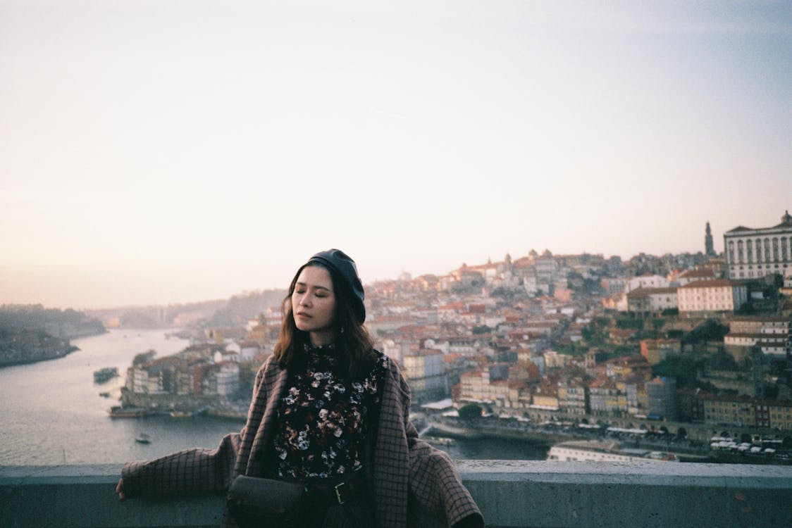 Woman in a plaid coat standing on a bridge overlooking the city