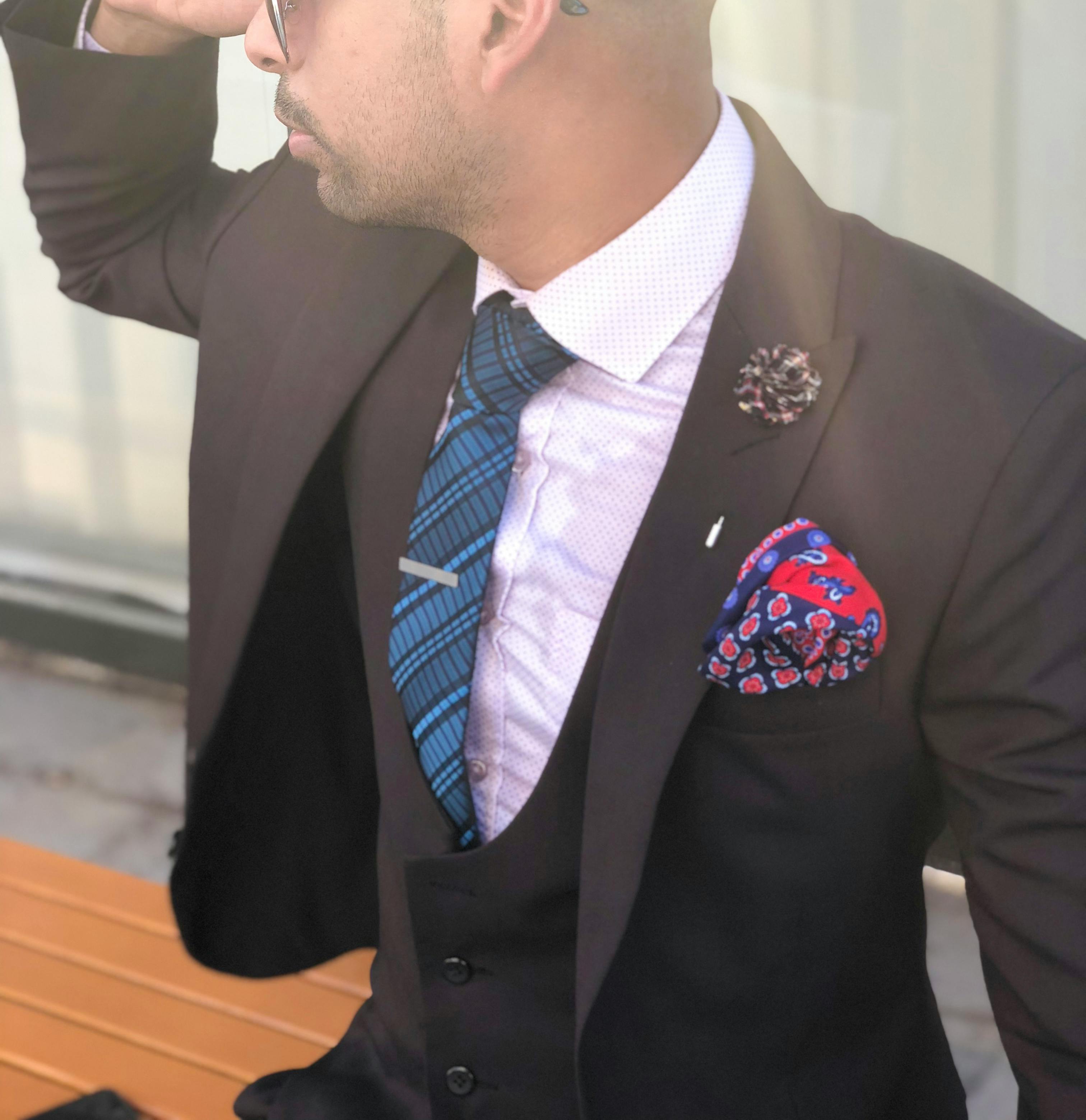 一位身着西装、戴着太阳镜的优雅男士在户外摆出姿势，展现时尚潮流