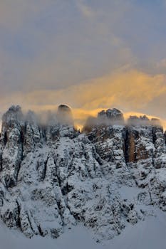 Majestic snow-covered peaks of Trentino-South Tyrol, Italy at sunrise, shrouded in mist.