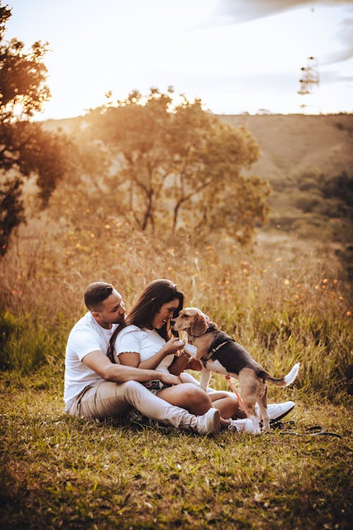 Photo of a Young Couple with a Dog Sitting on the Grass