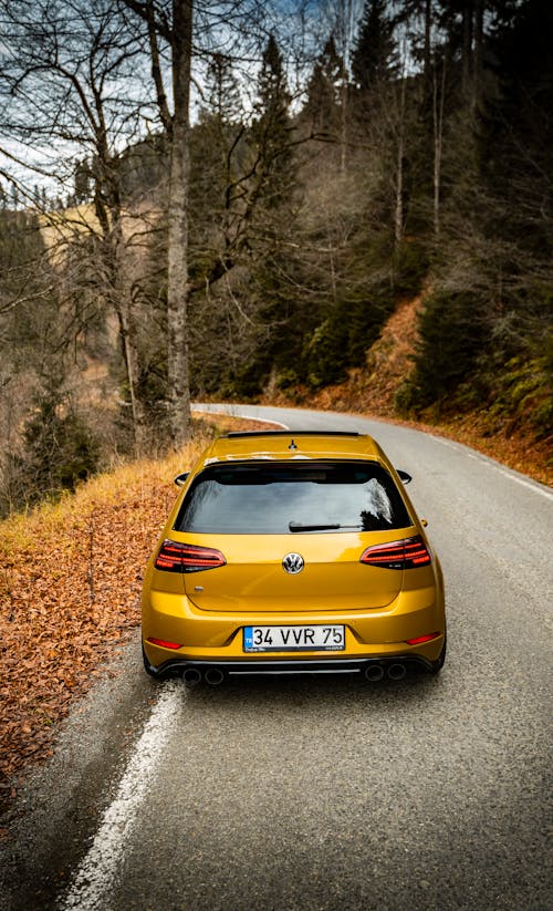 Back View of a Yellow Hatchback Car on the Road in the Mountains