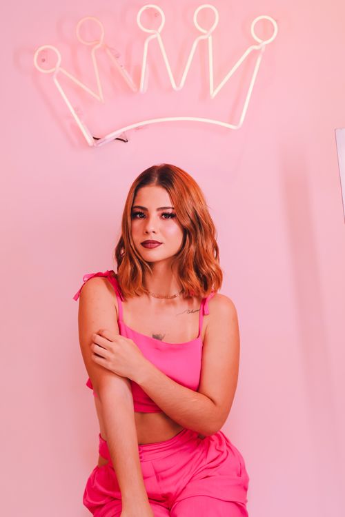 Free Portrait of a fashionable woman in a pink outfit with a neon crown backdrop. Stock Photo