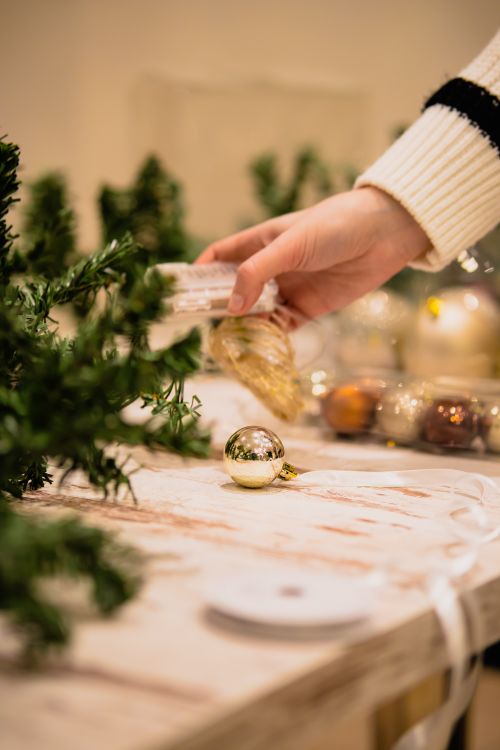 Free A hand decorates a Christmas tree with ornaments in a warm indoor setting. Stock Photo