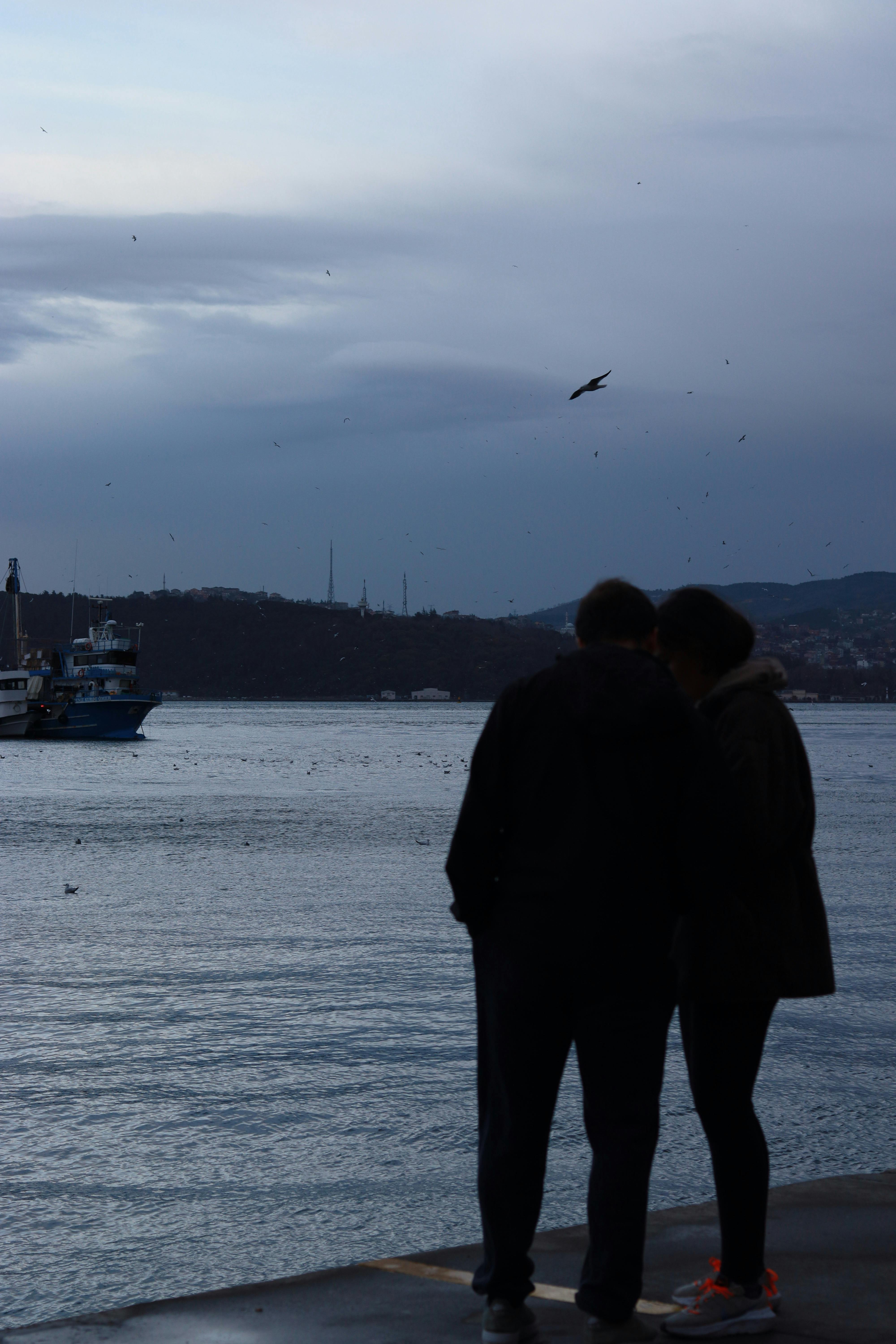 a couple is standing on the shore near a boat