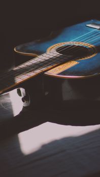 A close-up view of a blue acoustic guitar in natural light casting shadows.