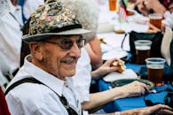 一位身穿节日服装、头戴帽子的微笑老人正与朋友一起享受啤酒节