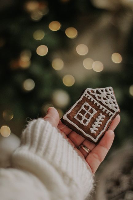 Close-up of a gingerbread cookie shaped like a house in a festive holiday setting with blurred lights.