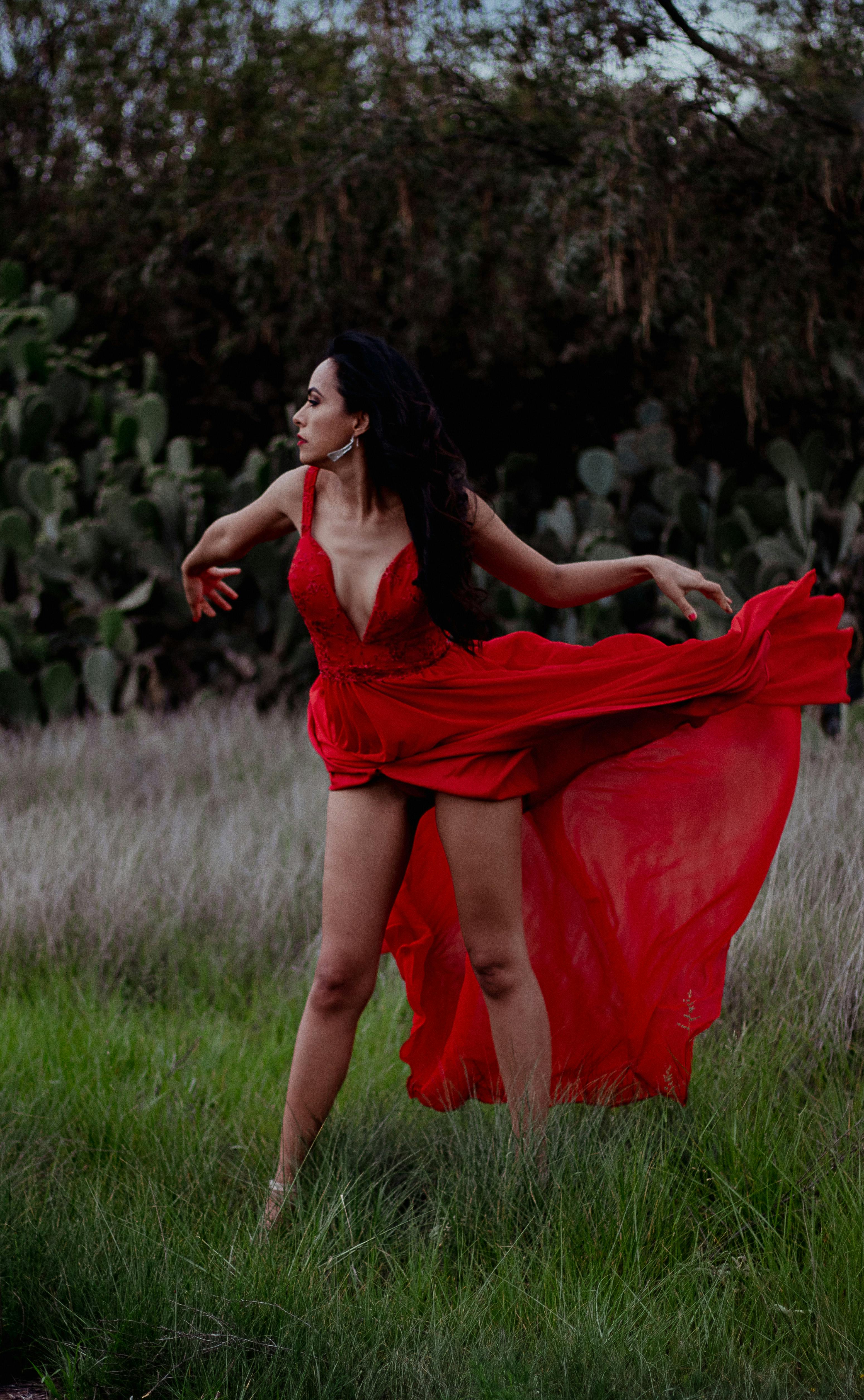 a woman in red long dress standing on green field while looking afar