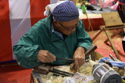 An elderly craftsman meticulously working on a wood project with traditional tools indoors.