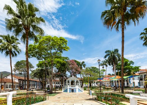 Free Scenic view of Praça Gomes Freire in Mariana, Brazil, featuring palm trees and historic townhouses under a vibrant summer sky. Stock Photo