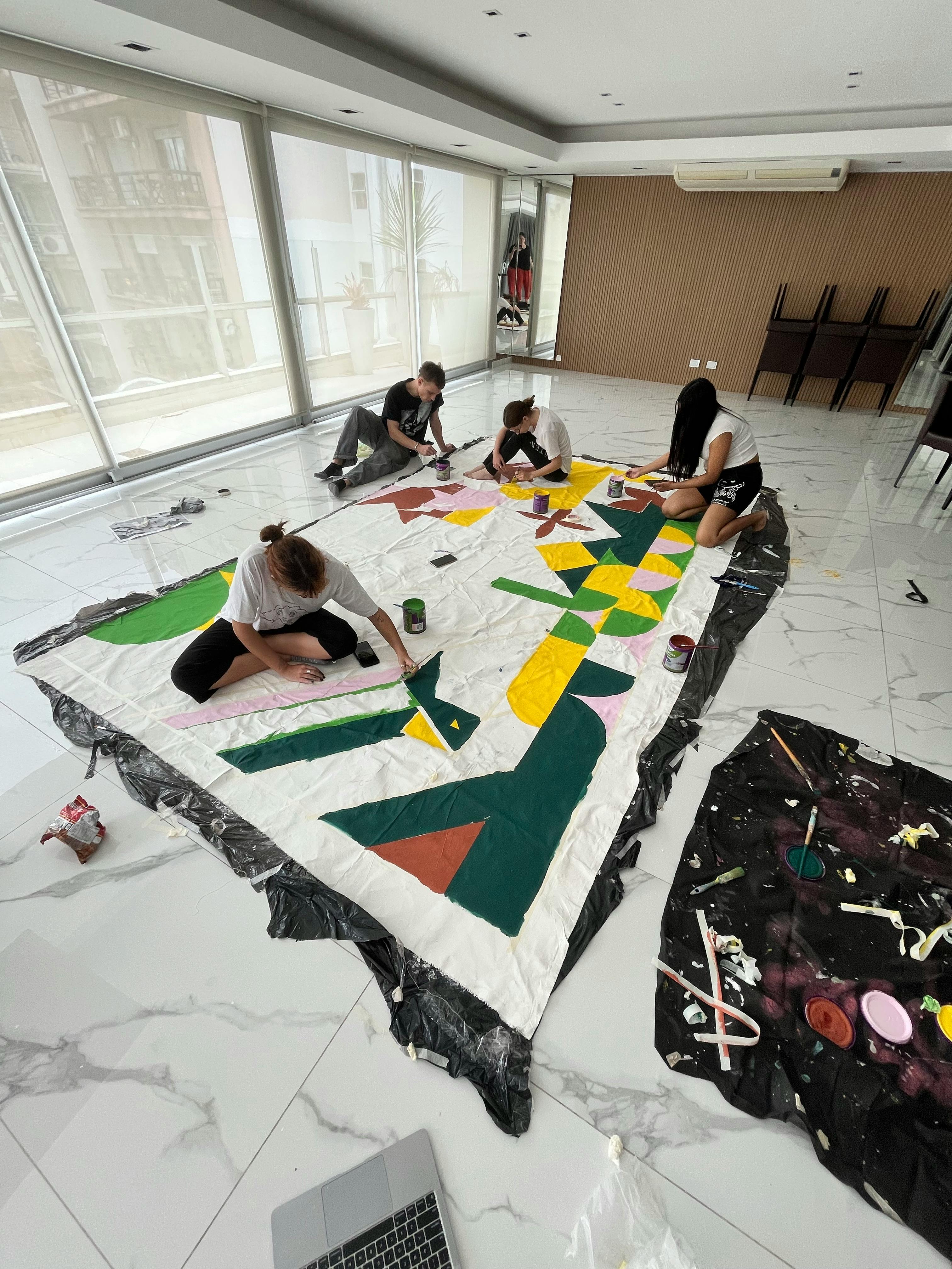 group of teenagers painting on a large canvas spread out on the floor