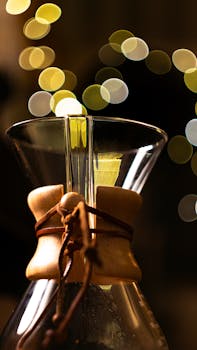 Elegant Chemex coffee maker with a warm bokeh light background, highlighting its classic pour-over design.