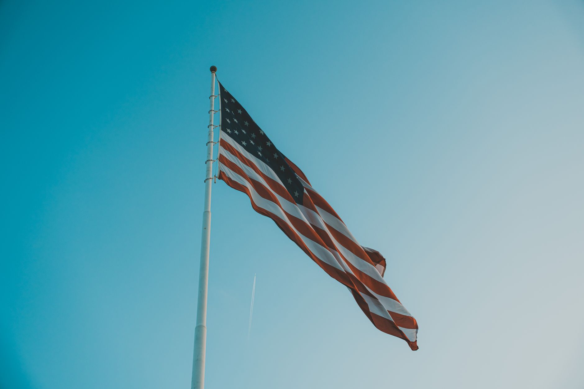 Low angle view of American flag waving on a flagpole against a bright clear sky.