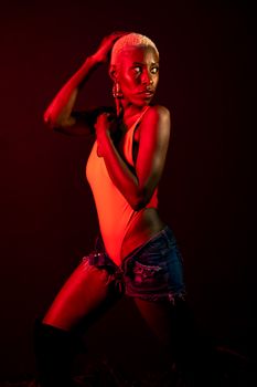 Dynamic pose of a woman in vibrant red lighting, wearing a bodysuit and denim shorts.