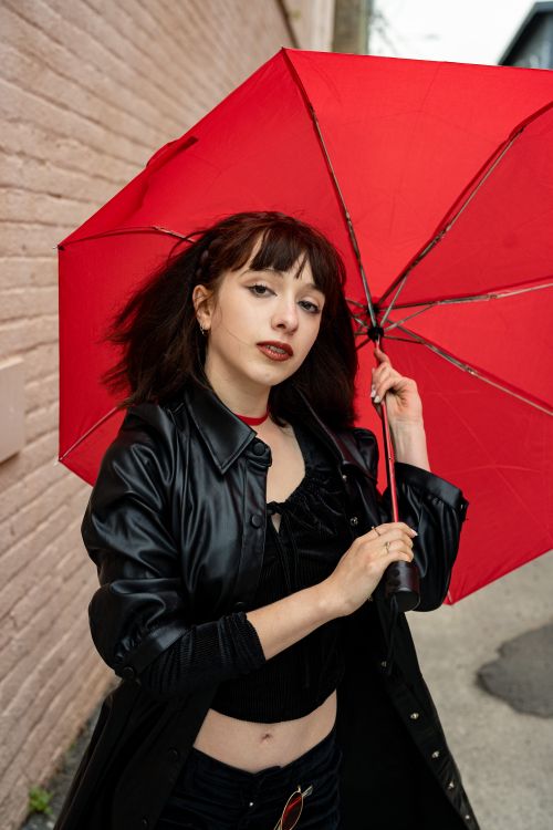 Free Young woman in black attire holding a vibrant red umbrella outdoors. Stock Photo