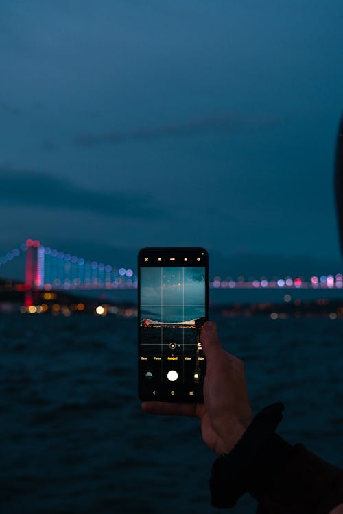 Hand Holding Phone and Photographing Sea and Bridge