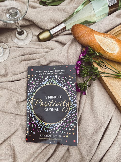3 Minute Positivity Journal Book on a Picnic Blanket Next to a Baguette and a Bottle of Champagne