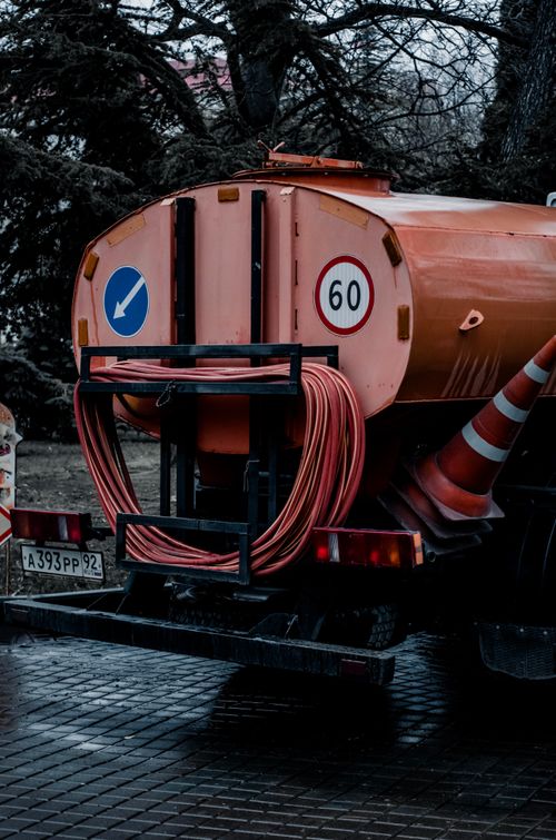 Free Orange service vehicle with hoses and traffic cones in an urban setting, depicting public utility work. Stock Photo
