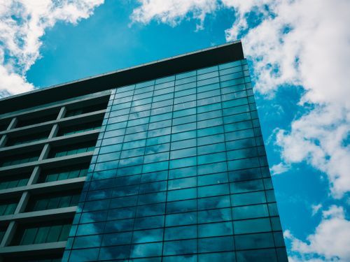 Free Low angle view of a modern glass building reflecting the sky, showcasing urban architecture. Stock Photo
