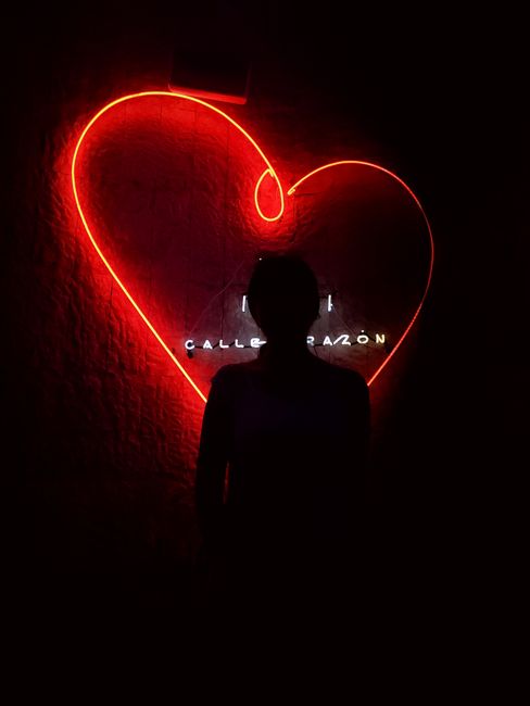 Silhouette posing against a glowing red neon heart sign in Playa del Carmen.