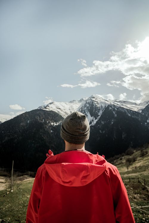 Free Man in a red coat gazes at the snowy peaks of the Kackar Mountains in Rize, Türkiye. Stock Photo