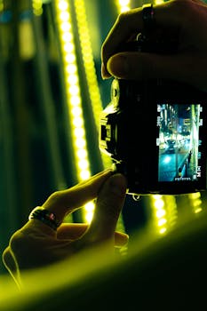 A photographer's hands holding a camera, focusing on city night lights. Artistry in action.