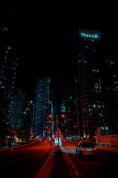 Night view of Dubai's skyscrapers with illuminated Emaar building, vibrant city lights and urban streets.