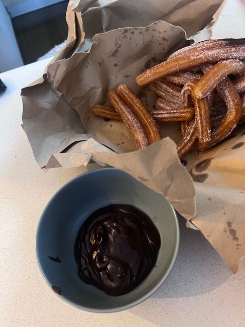 Close-up of crispy churros served with a bowl of rich chocolate sauce on a paper wrap.