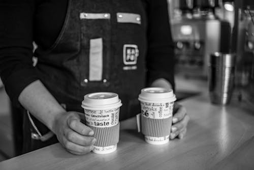 Grayscale Photo of Person Holding Disposable Cups