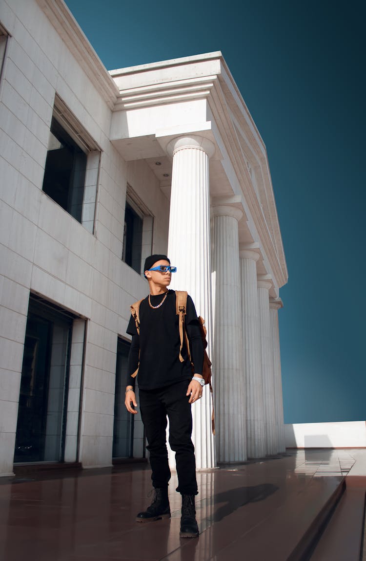 A Man In Black Long Sleeves And Pants Standing Near The Building With Pillars While Looking Over Shoulder