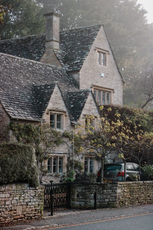 Free Cozy stone cottage surrounded by lush trees and mist, capturing serene rural life. Stock Photo