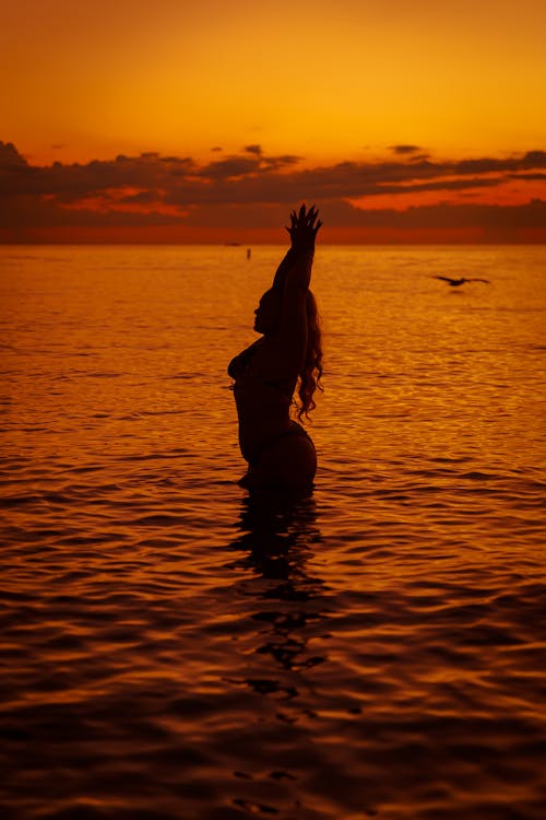 Silhouette of Woman Standing in the Sea at Sunset 