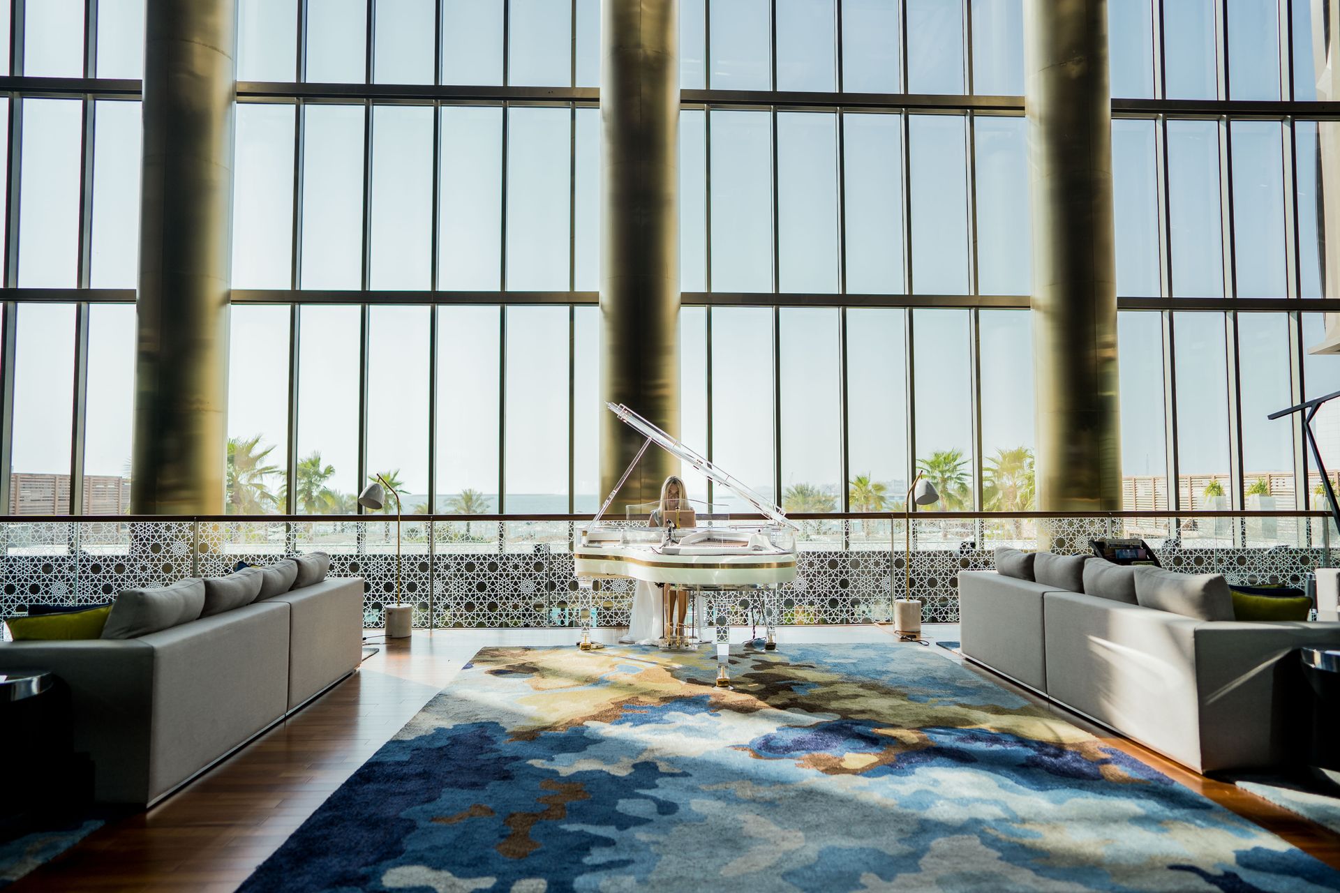 A modern hotel lobby in Dubai featuring a grand piano, plush sofas, and large windows offering a stunning view.