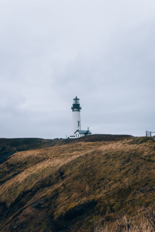 Free A picturesque lighthouse stands on a windswept cliff under a cloudy sky, capturing the essence of coastal solitude. Stock Photo