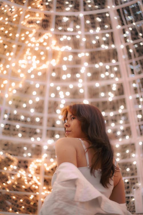 Low Angle Shot of a Woman Standing Near Hanging String Lights while Looking Afar