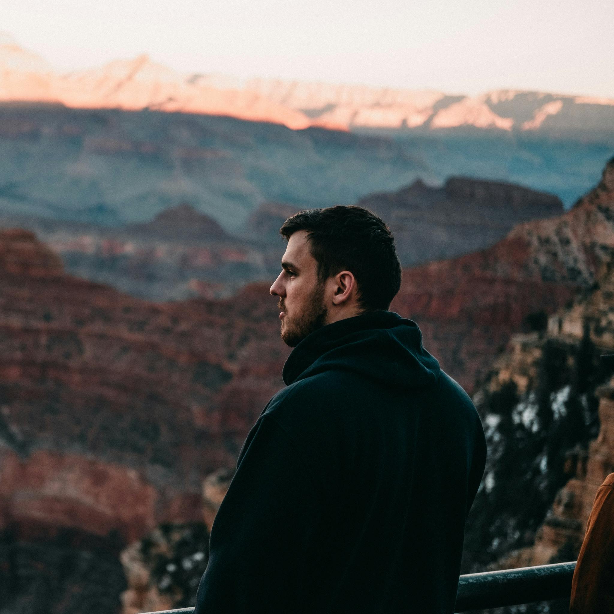 A man in a black hoodie gazes over the Grand Canyon at sunset, capturing a tranquil moment.