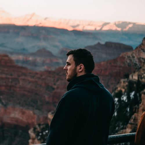 Free A man in a black hoodie gazes over the Grand Canyon at sunset, capturing a tranquil moment. Stock Photo