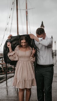 Couple sharing a jacket during rain on a dock, showcasing elegance and care.