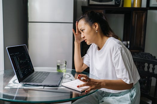 Woman worriedly analyzing stock market data on laptop at home, indicating financial stress.