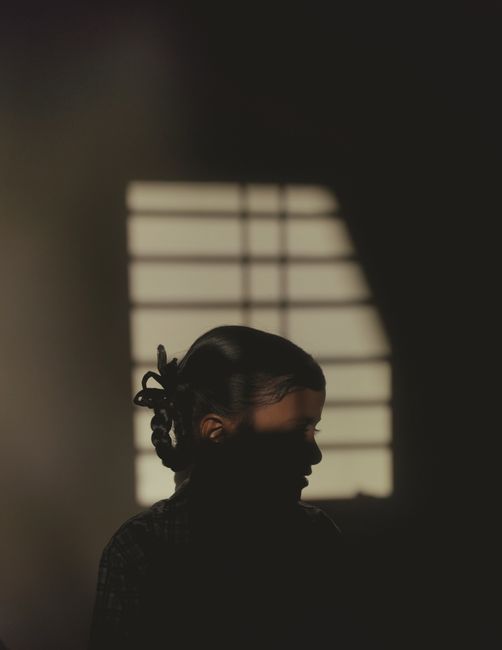A dramatic silhouette of a woman against a window-lit room with soft light and shadows.
