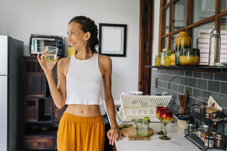 Woman Standing In The Kitchen With A Glass In Hand And Smiling 