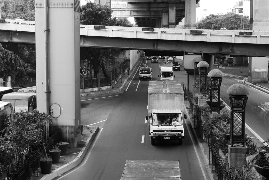Monochrome street view of a busy urban road with vehicles under an overpass.