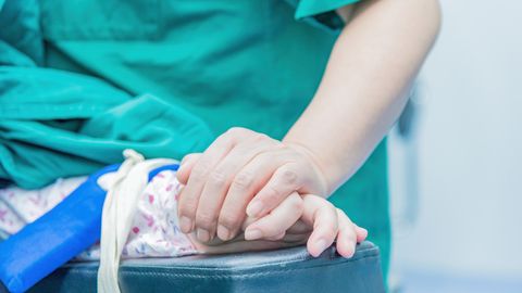 Medical professional comforting a patient by holding hands in an operating room setting.