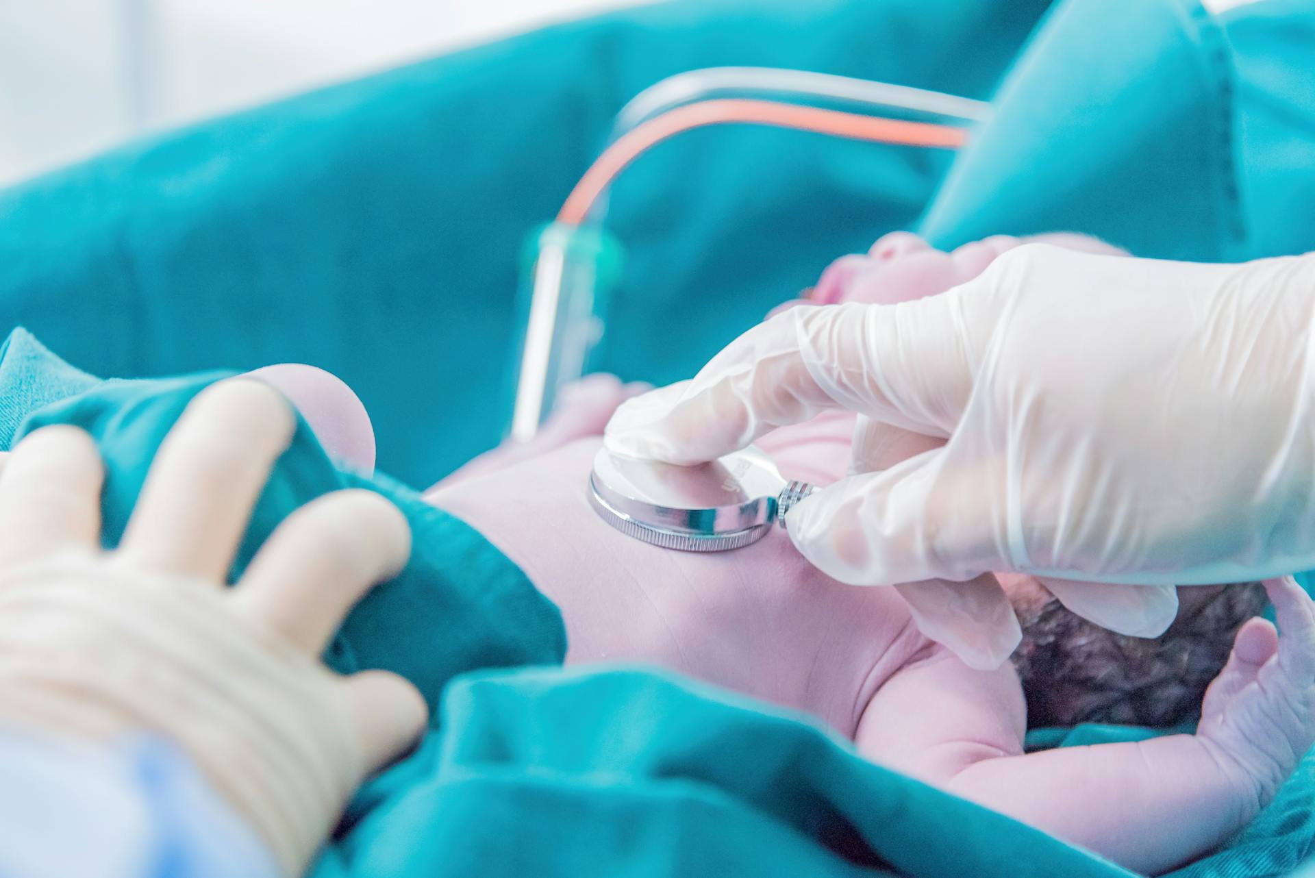 Medical professional examining a newborn baby with a stethoscope in a hospital setting.