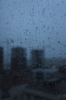 Rain droplets on a window with a blurred view of city buildings, creating a moody atmosphere.