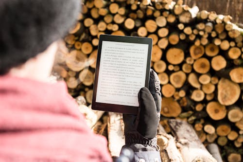 Free Person Holding Black E-book Reader Near Pile of Firewood Stock Photo