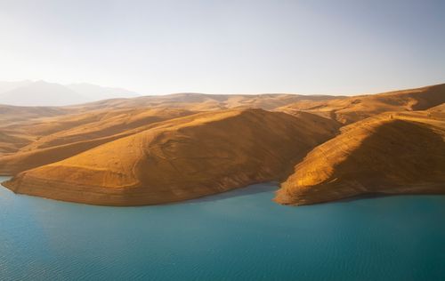 Free A breathtaking aerial view captures arid hills surrounding a serene blue body of water, illustrating nature's tranquility. Stock Photo